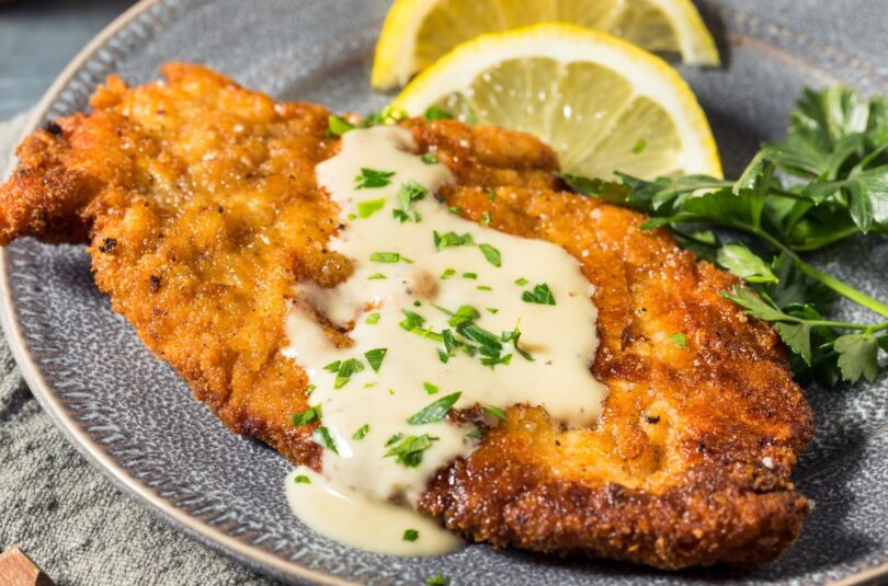 Goldbraun panierte Hähnchenschnitzel auf einem Teller, daneben frische Zitronenspalten