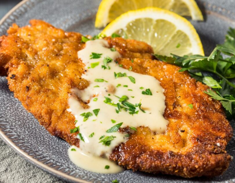 Goldbraun panierte Hähnchenschnitzel auf einem Teller, daneben frische Zitronenspalten