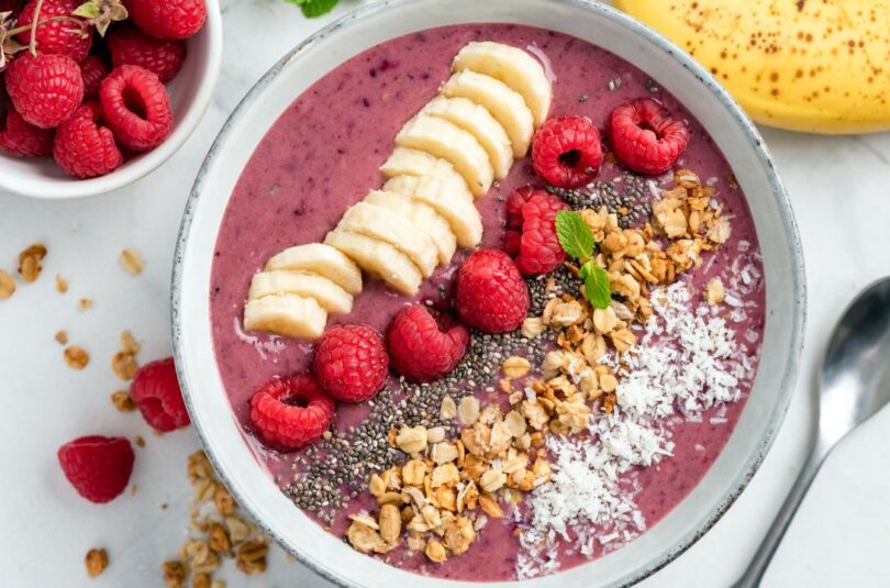 Lila-farbene Smoothie Bowl garniert mit Granola, Kokosflocken und frischen Früchten