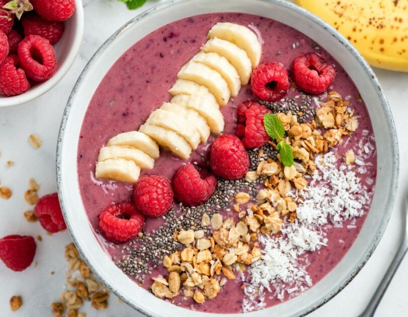 Lila-farbene Smoothie Bowl garniert mit Granola, Kokosflocken und frischen Früchten