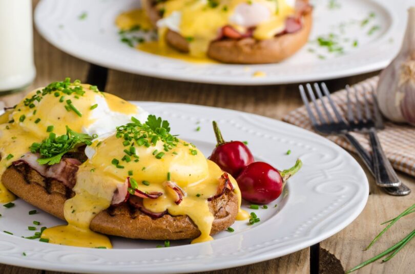 Eggs Benedict mit pochierten Eiern, knusprigem Bacon und cremiger Sauce Hollandaise, serviert auf gerösteten englischen Muffins.