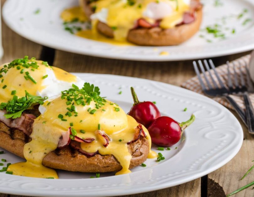 Eggs Benedict mit pochierten Eiern, knusprigem Bacon und cremiger Sauce Hollandaise, serviert auf gerösteten englischen Muffins.