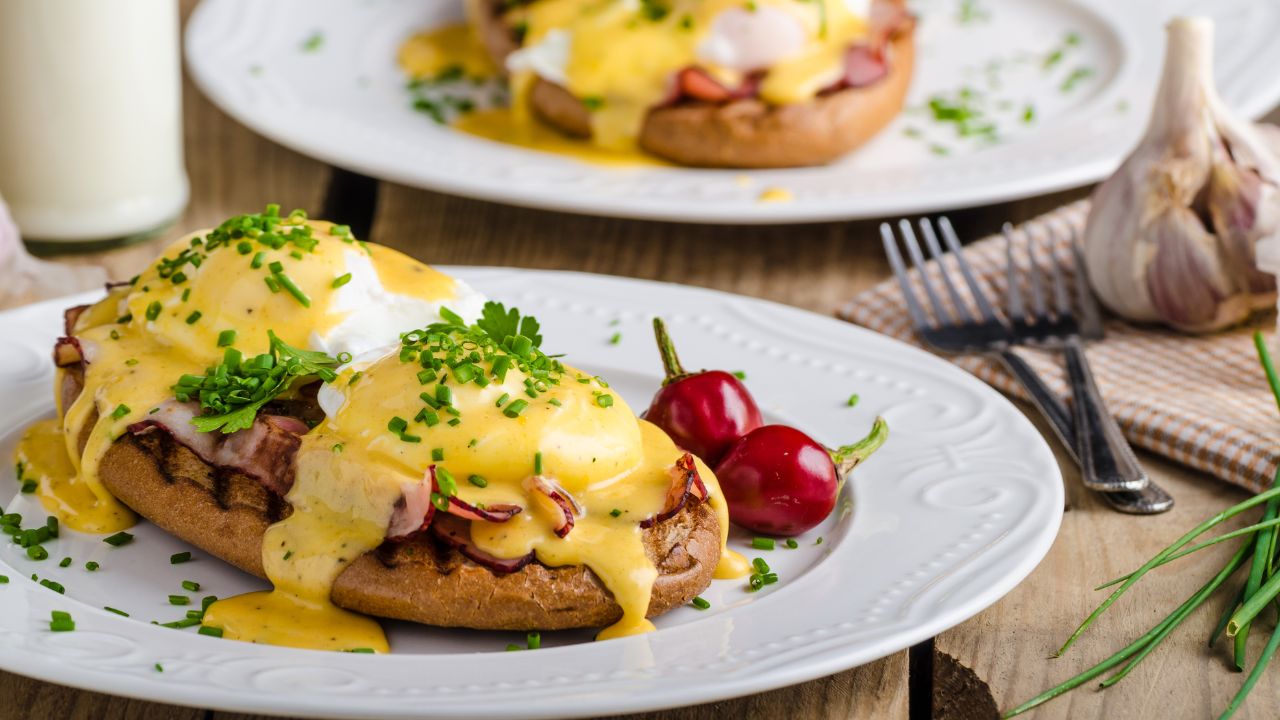 Eggs Benedict mit pochierten Eiern, knusprigem Bacon und cremiger Sauce Hollandaise, serviert auf gerösteten englischen Muffins.