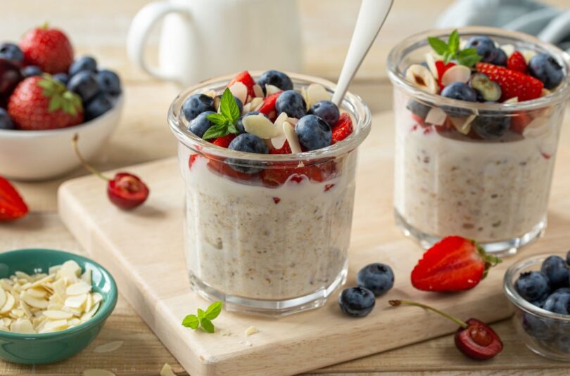 Overnight Oats in einem Glas serviert mit frischen Beeren und Mandeln Description: Cremige Overnight Oats mit frischen Beeren, Chiasamen und gehackten Mandeln in einem Glas angerichtet