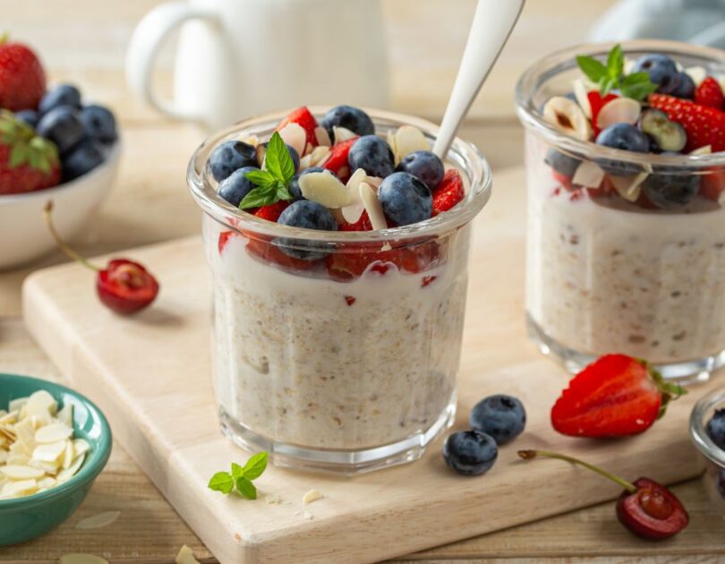 Overnight Oats in einem Glas serviert mit frischen Beeren und Mandeln Description: Cremige Overnight Oats mit frischen Beeren, Chiasamen und gehackten Mandeln in einem Glas angerichtet