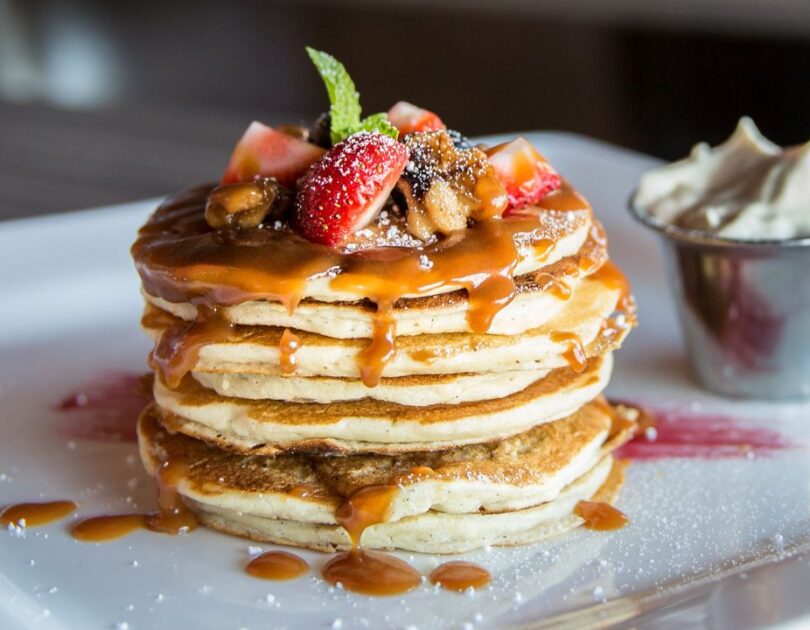 Stapel goldbrauner, fluffiger Buttermilch Pancakes mit Ahornsirup und frischen Beeren